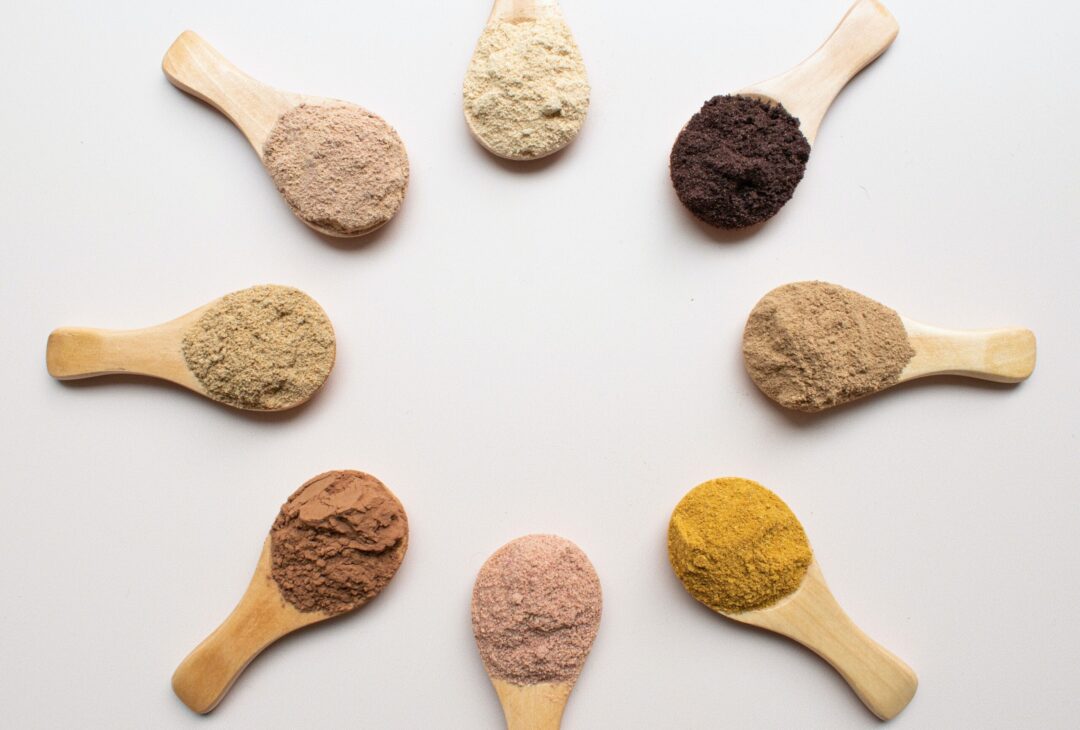 8 small wooden spoons in a circle with different protein powders on them